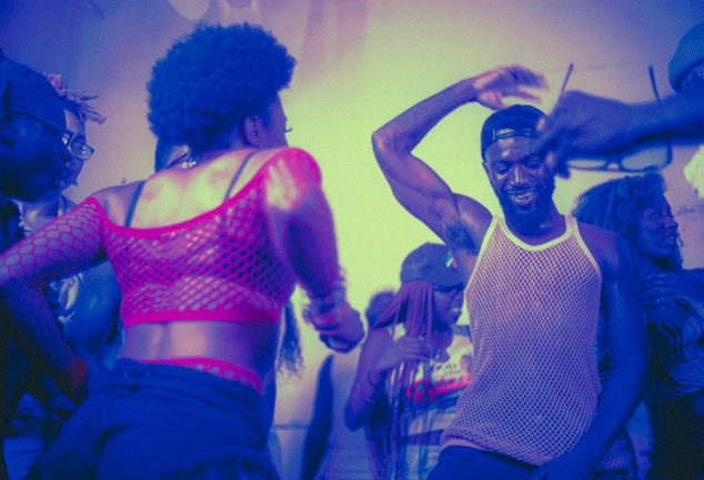 Black male and females dressed in trendy clothes dancing at club.