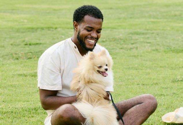 Black man in field playing with a dog.