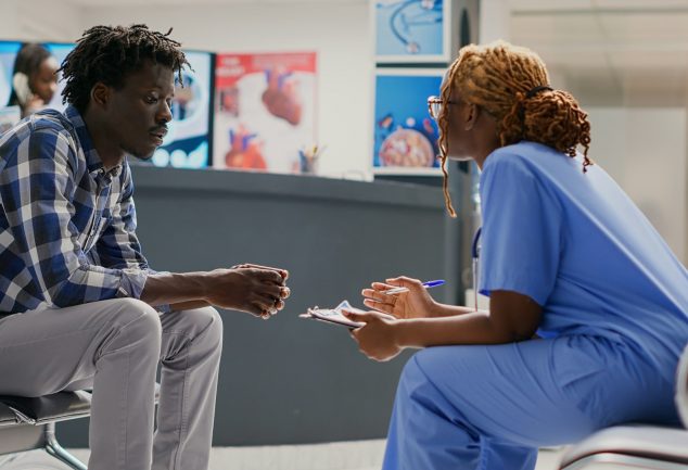Black man sitting in healthcare facility consulting a Black female caregiver